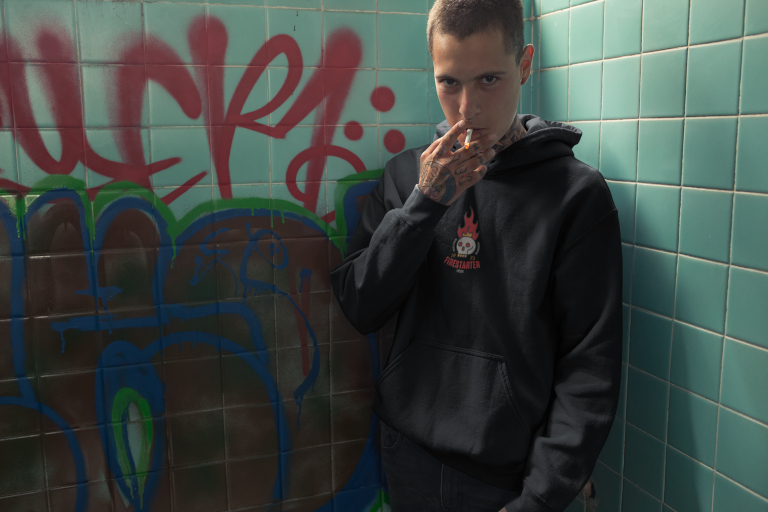 A punk rock man smoking a cigarette wearing a Brand X Firestarter Hoodie